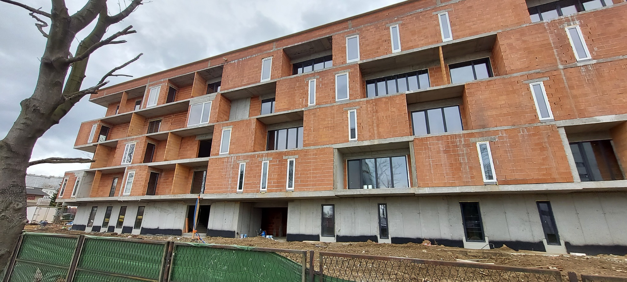 Wielopiętrowy budynek w stanie surowym otwartym z zamontowanymi oknami, widok z dołu, szare niebo w tle.