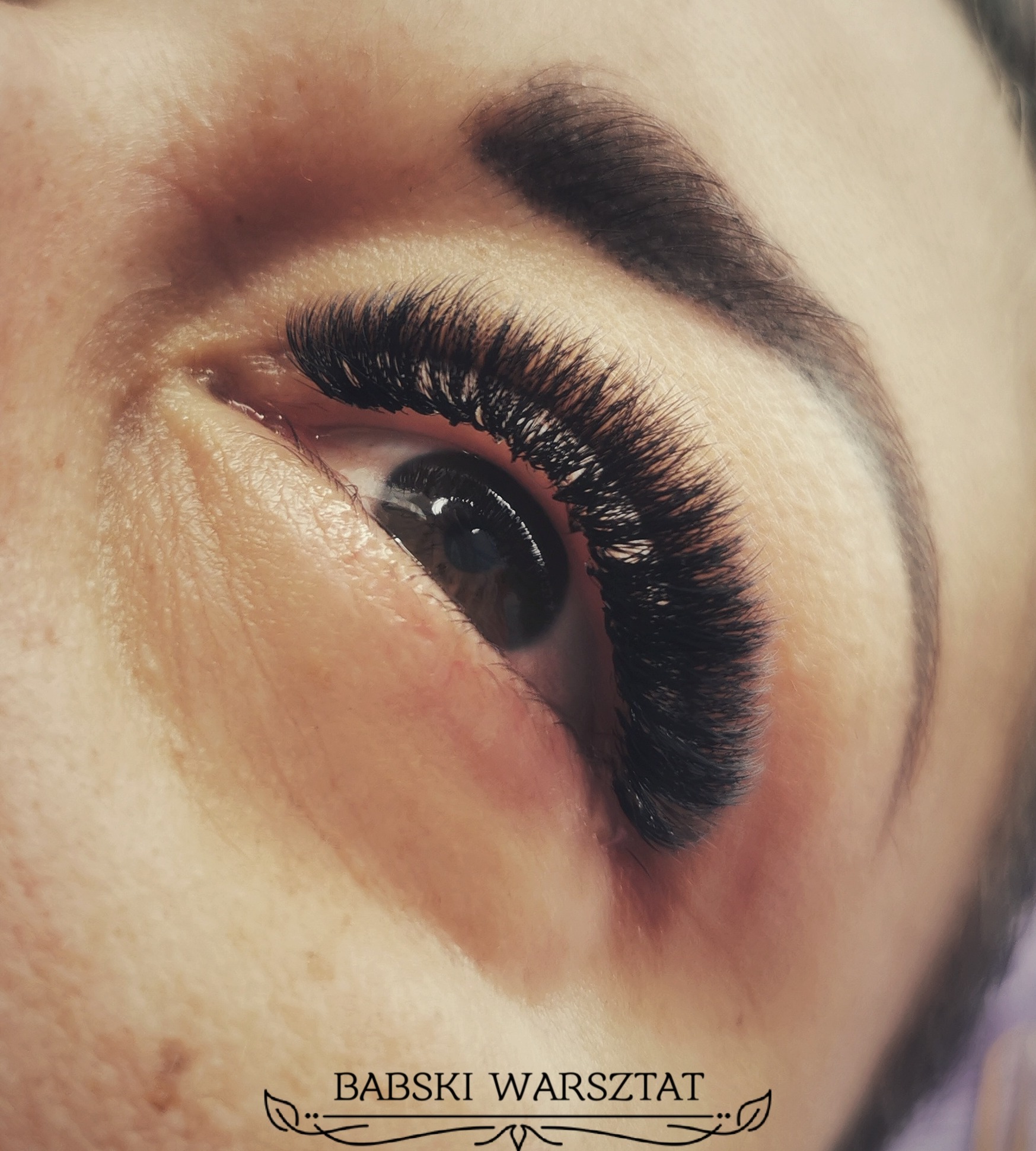 Zbliżenie na oko z przedłużonymi, bardzo gęstymi, czarnymi rzęsami w stylu 'russian volume', widoczna brązowa tęczówka i naturalna brew.