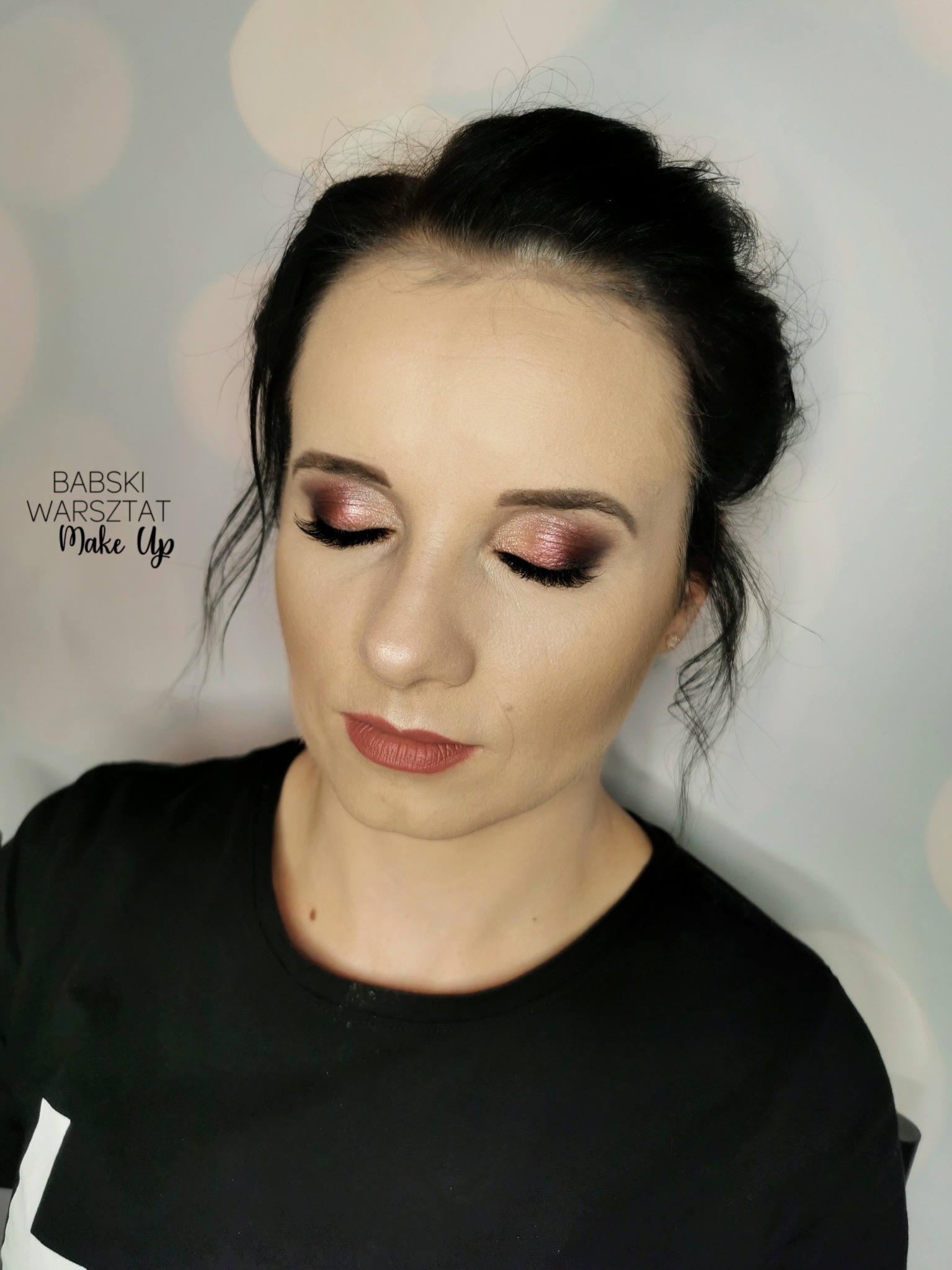 Portret kobiety z zamkniętymi oczami prezentującej makijaż oczu w odcieniach różu i brązu, wykonany w salonie w Pisz. Widoczny delikatny makijaż ust i upięte włosy.