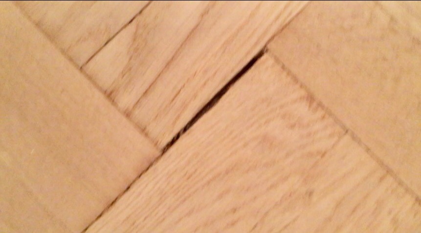 Parkiet dębowy ułożony w jodełkę z widoczną szczeliną między klepkami.