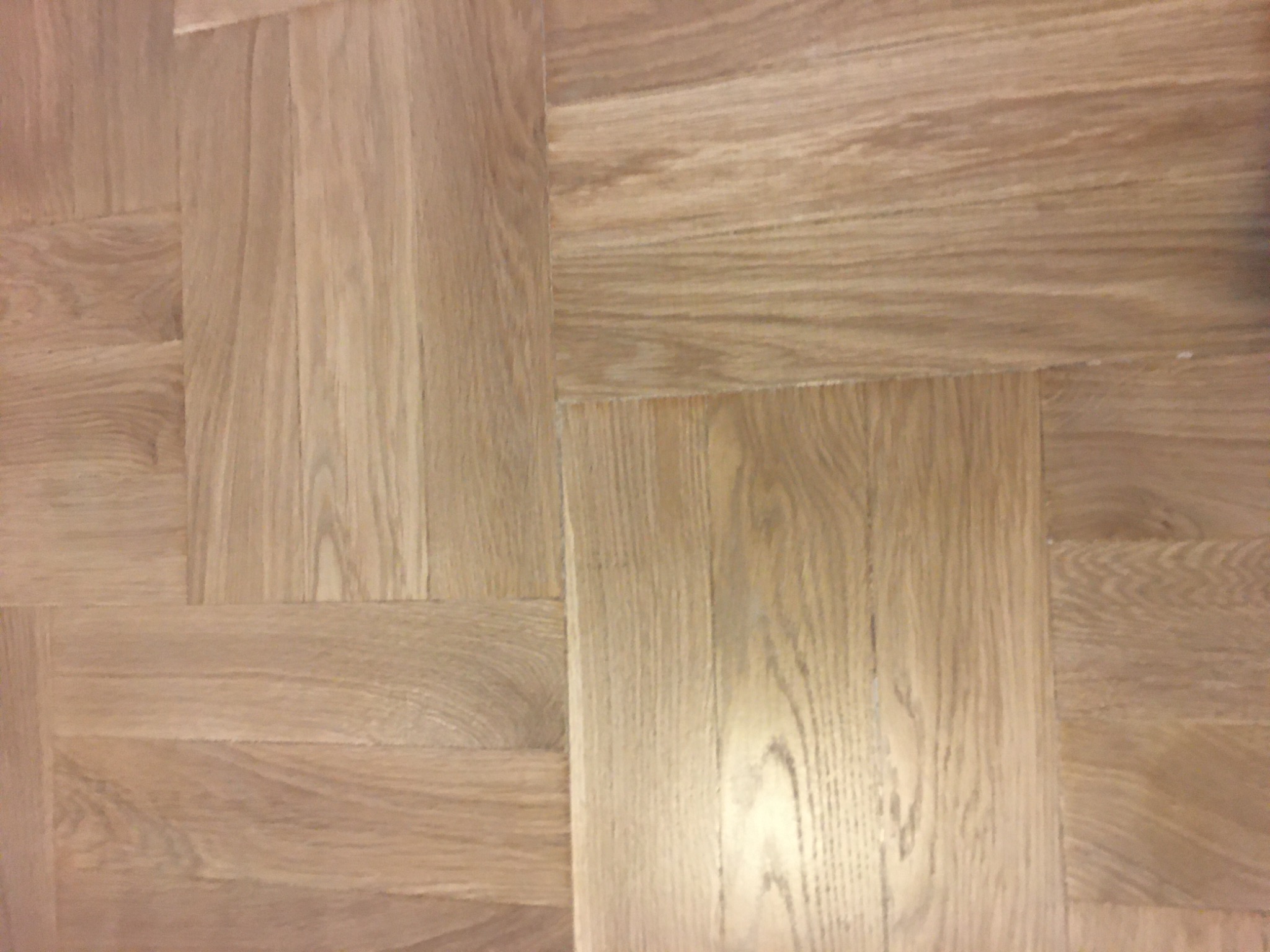 Parkiet ułożony w jodełkę francuską, z widocznymi słojami drewna i delikatnym połyskiem lakieru.