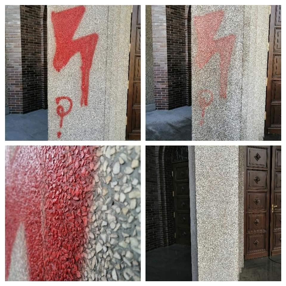 Elewacja z kamyczkową fakturą z czerwonym graffiti w kształcie błyskawicy i znaku zapytania, widoczne ceglane elementy budynku i drewniane drzwi.