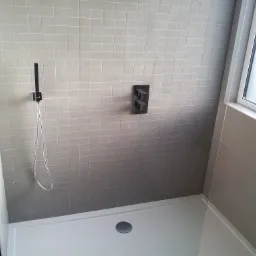 Nowoczesna kabina prysznicowa z szarymi, kwadratowymi płytkami, czarną armaturą i odpływem liniowym.