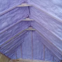Poddasze z drewnianą konstrukcją pokryte warstwą jasnofioletowej pianki izolacyjnej, widok z dołu.