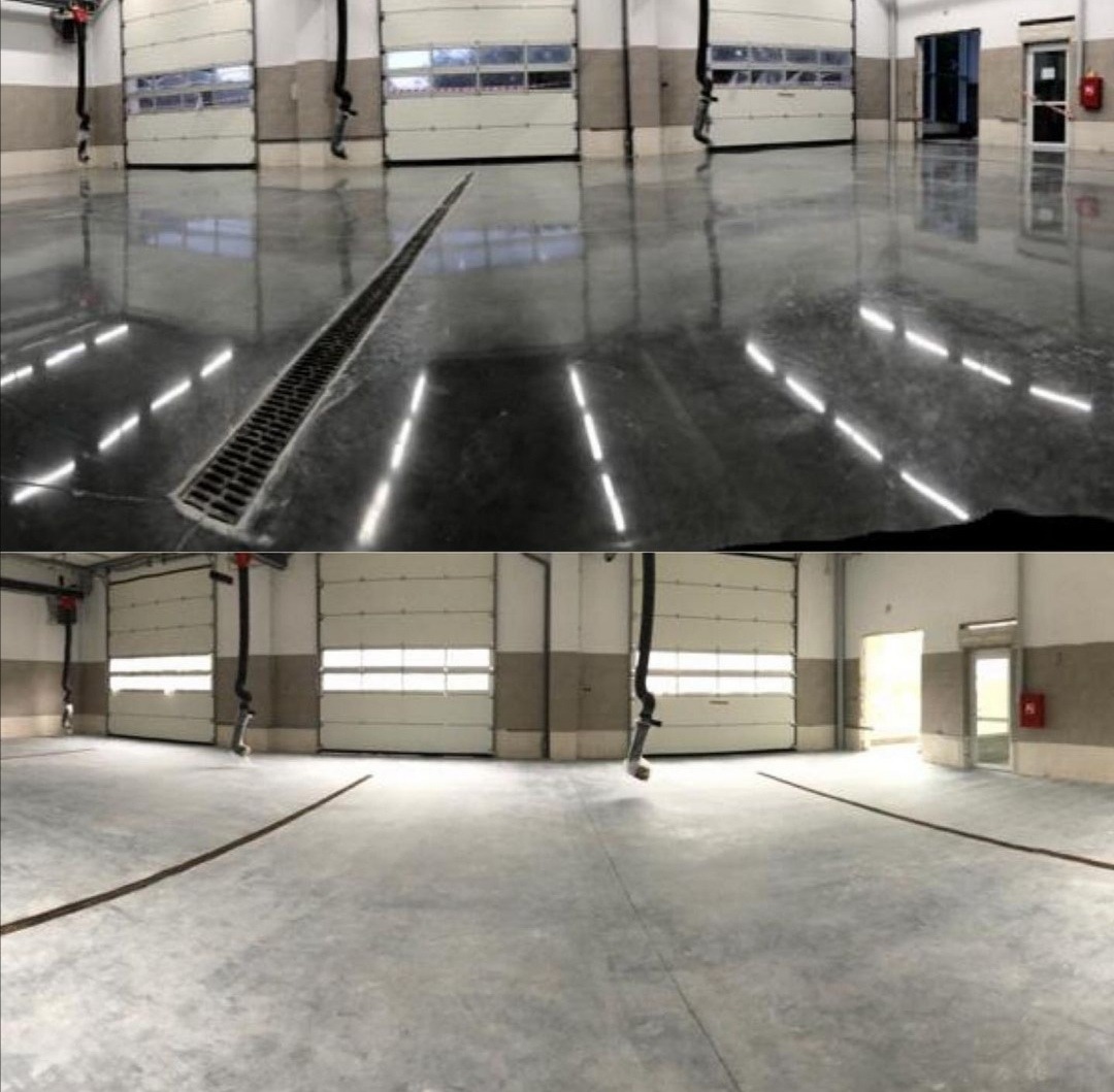 Wnętrze hali przemysłowej z gładką, szarą posadzką i systemem odprowadzania wody w postaci kratki ściekowej, widoczne bramy segmentowe z oknami i hydrant.