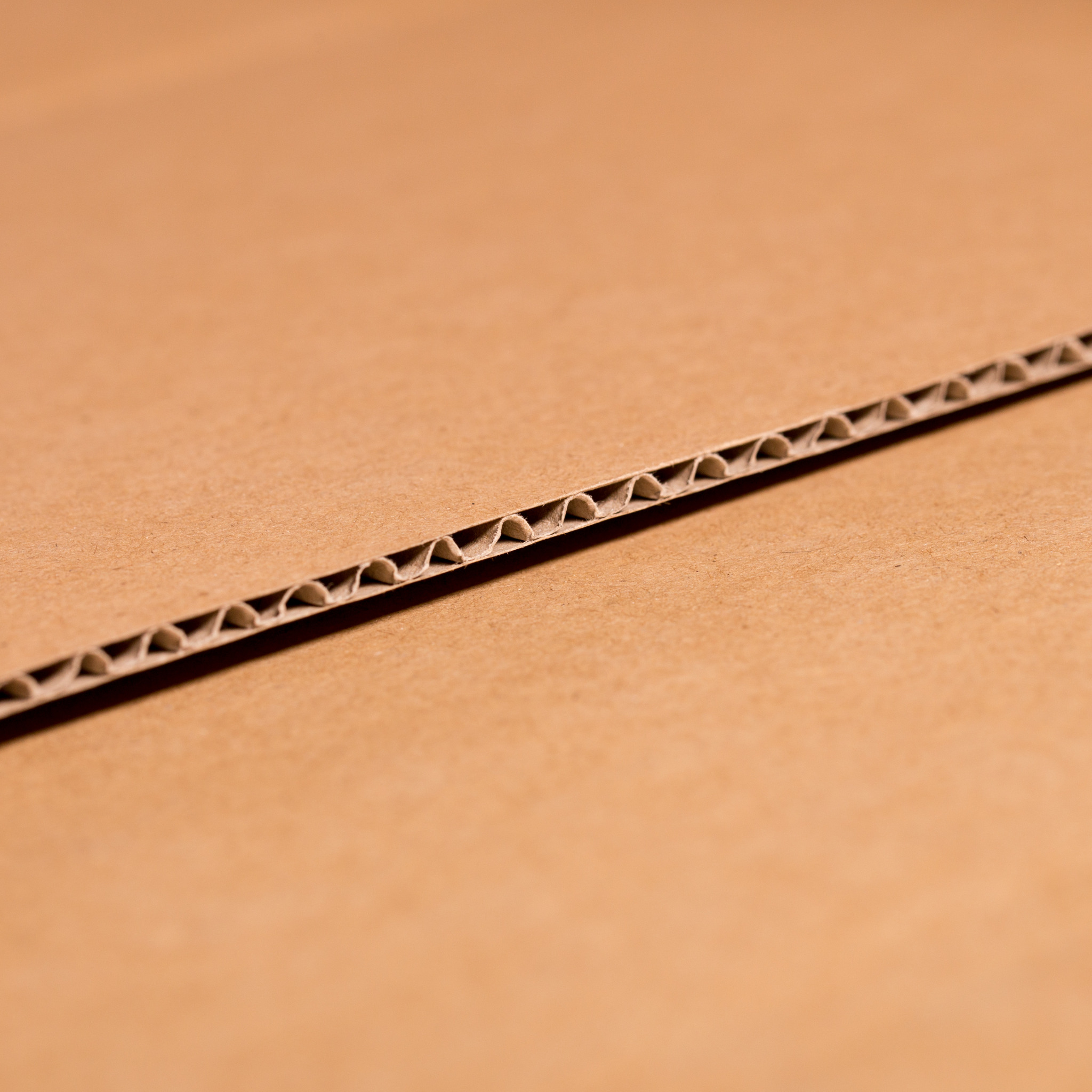 Przekrój brązowego kartonu falistego, ukazujący strukturę warstw i fal.