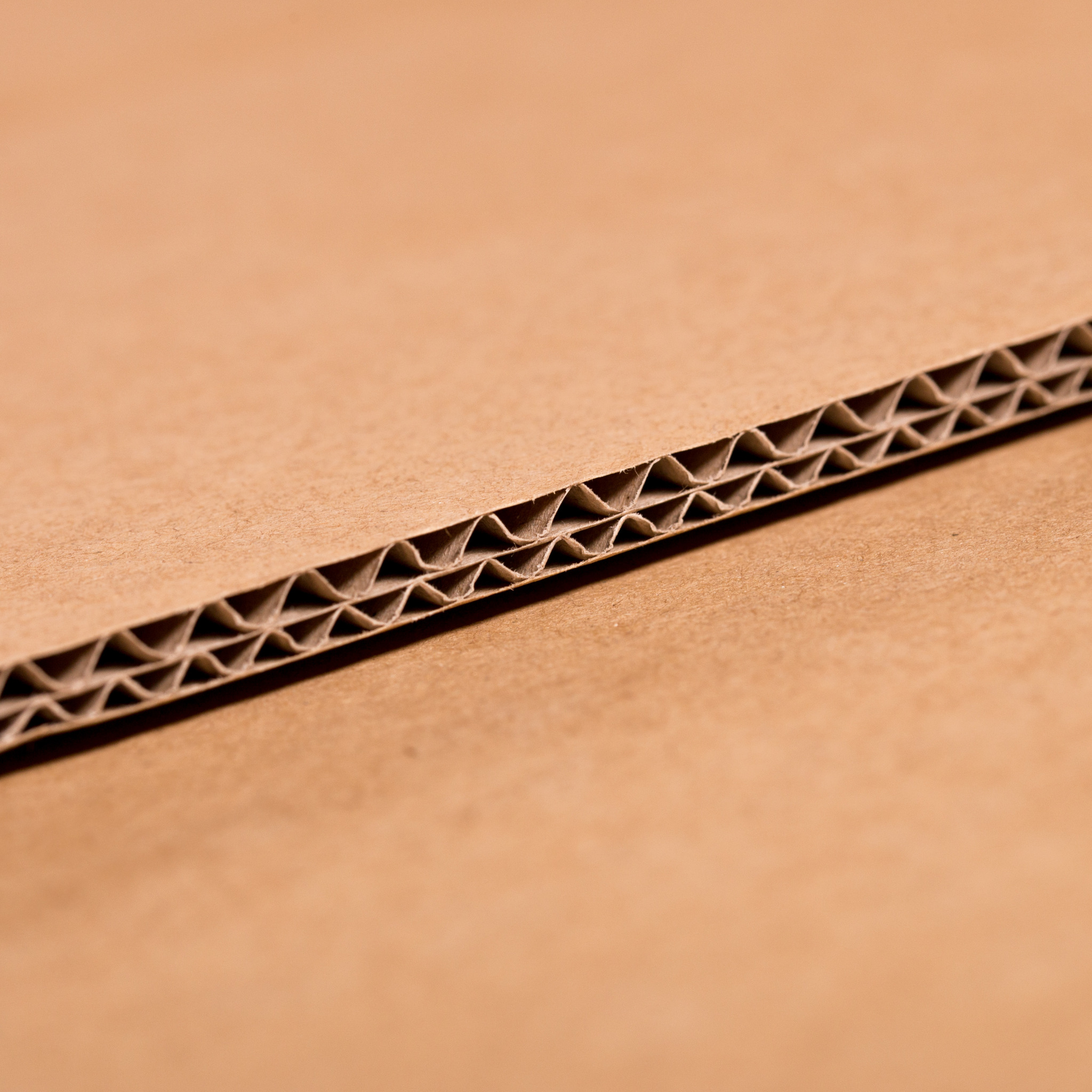 Przekrój brązowego, trójwarstwowego kartonu falistego ukazujący jego strukturę, z widoczną falą między dwiema płaskimi warstwami.