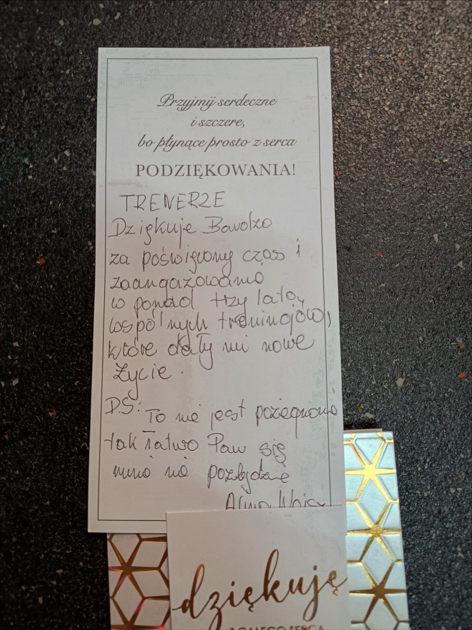 Podziękowanie dla trenera napisane odręcznie na kartce z życzeniami, podkreślające poświęcony czas i zaangażowanie w treningi, które dały nowe życie, obok kartka z napisem 'dziękuję'.