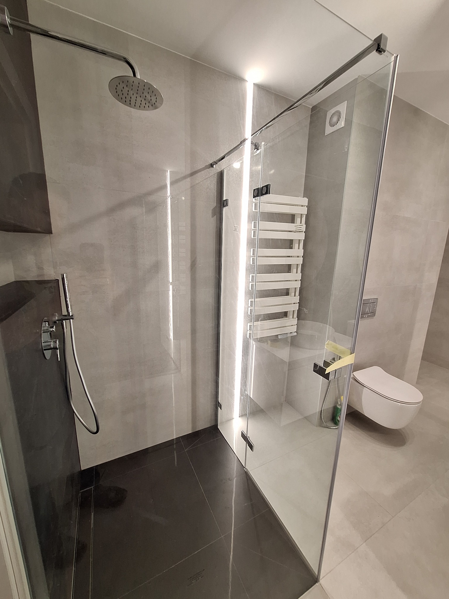 Nowoczesna łazienka z kabiną prysznicową typu walk-in, czarną posadzką i grzejnikiem drabinkowym w tle.