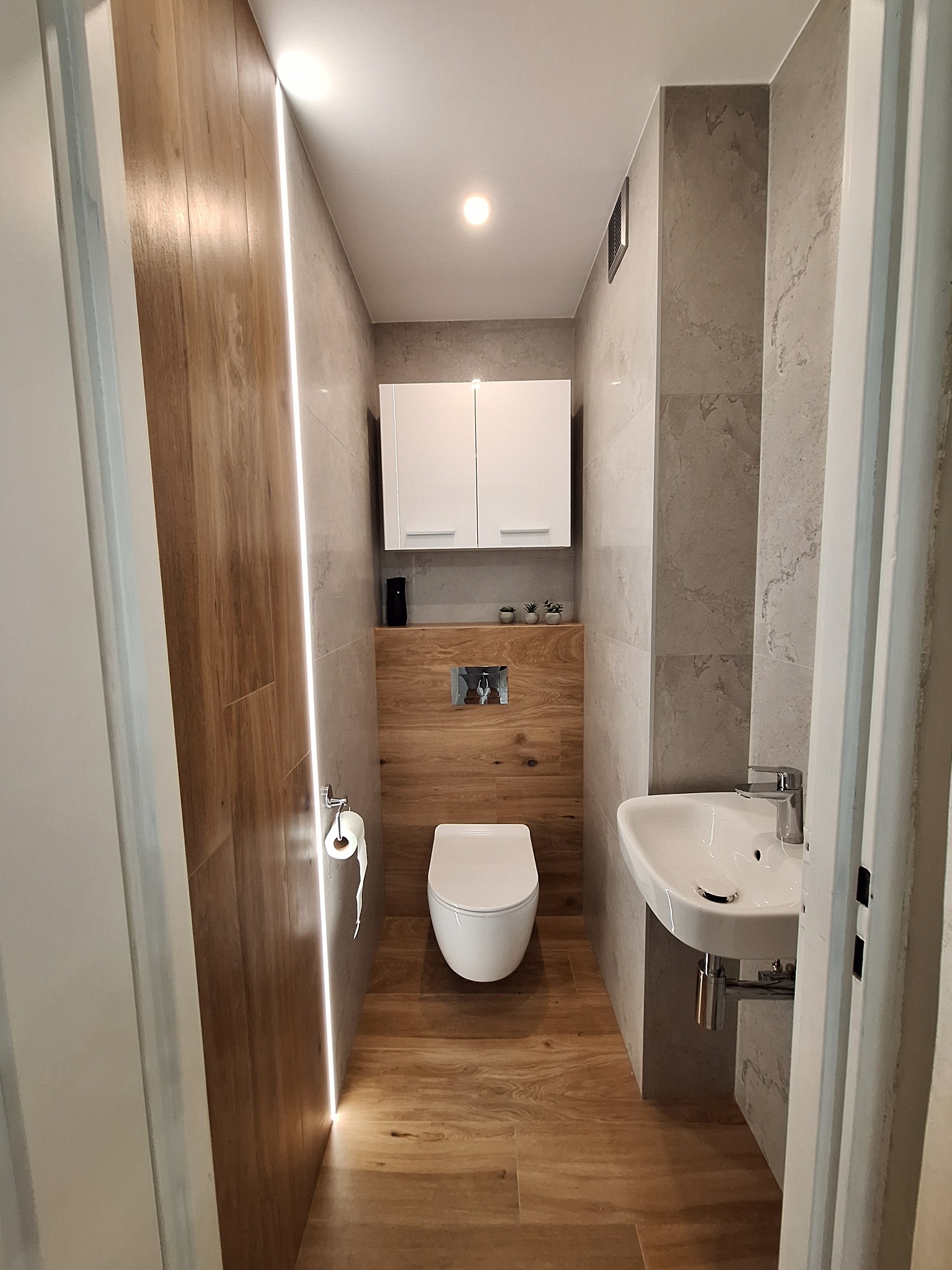 Nowoczesna toaleta z drewnianą okładziną, podświetleniem LED, umywalką nablatową i podwieszaną miską WC.