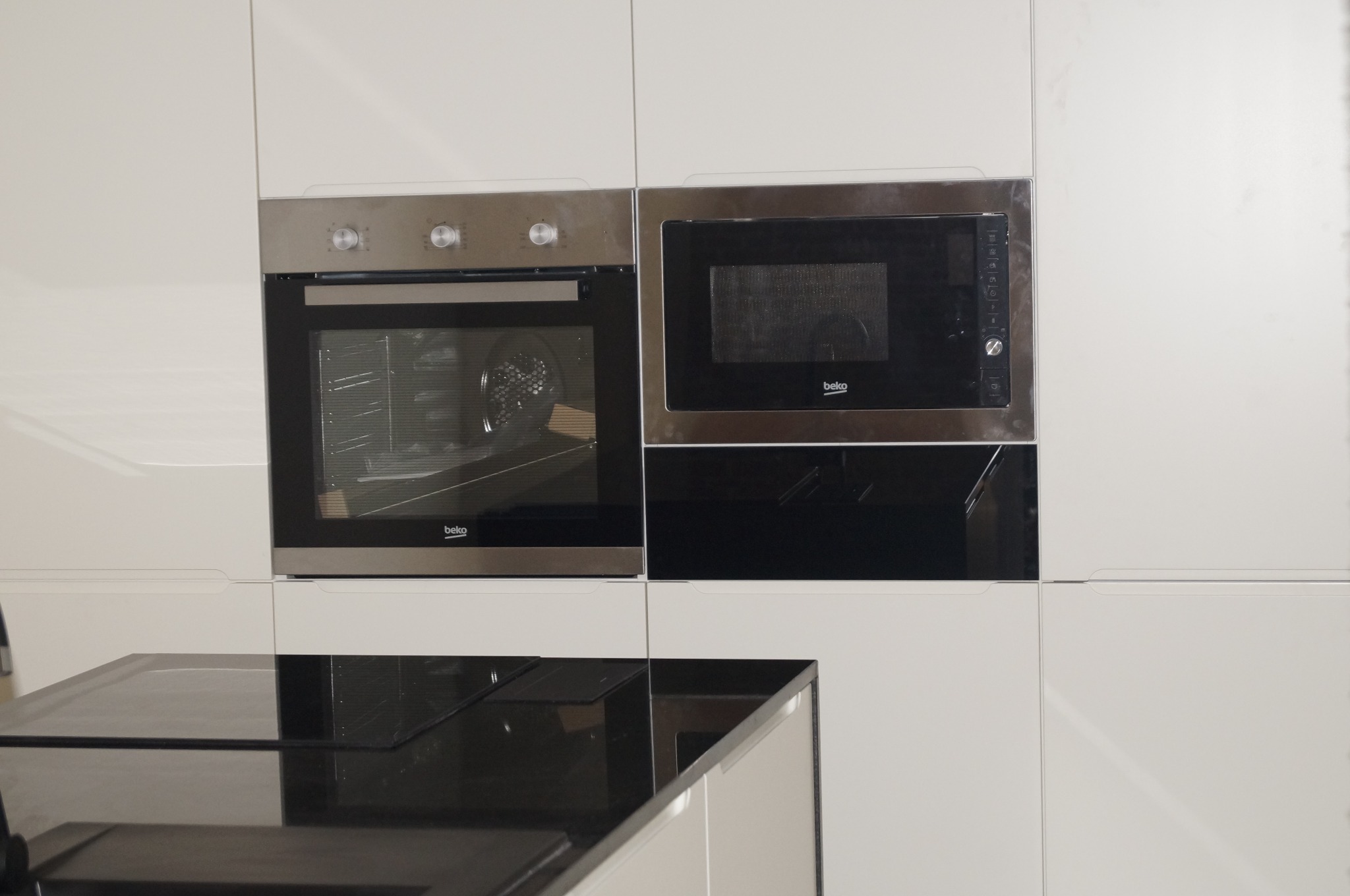 Biała zabudowa kuchenna z piekarnikiem i mikrofalówką marki Beko, czarny blat, zrealizowana w Myczkowie.