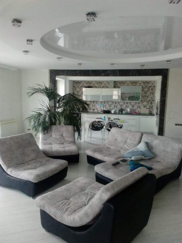 Jasne wnętrze salonu z aneksem kuchennym, z nowoczesnymi meblami wypoczynkowymi i podwieszanym sufitem z oświetleniem punktowym.