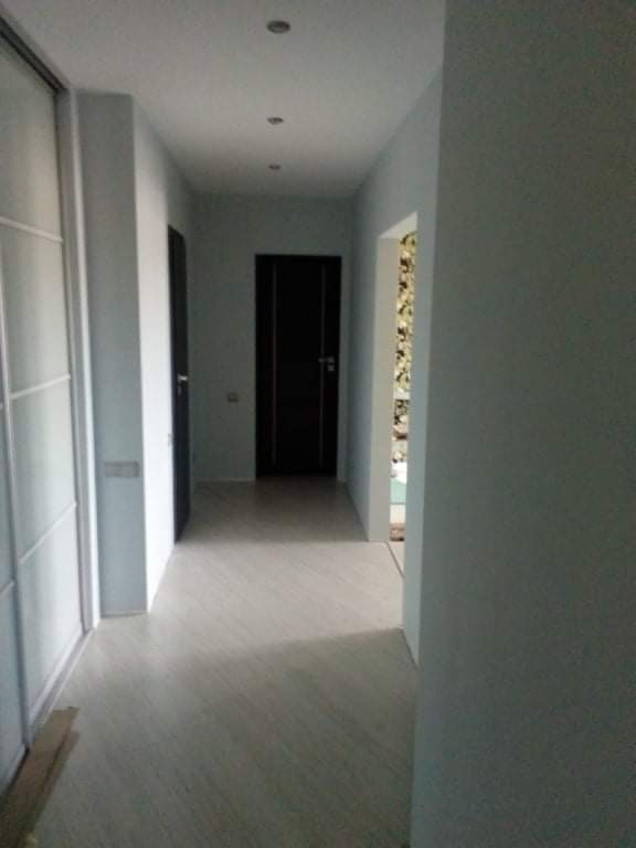 Wnętrze korytarza po odświeżeniu, ściany w odcieniach szarości, panele podłogowe imitujące drewno, sufit z punktowym oświetleniem, widoczne drzwi w kolorze czarnym.