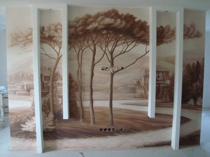 Malowidło ścienne przedstawiające pejzaż toskański z drzewami, budynkami i drogą, wykonane w odcieniach brązu i beżu, z białymi pionowymi elementami architektonicznymi.
