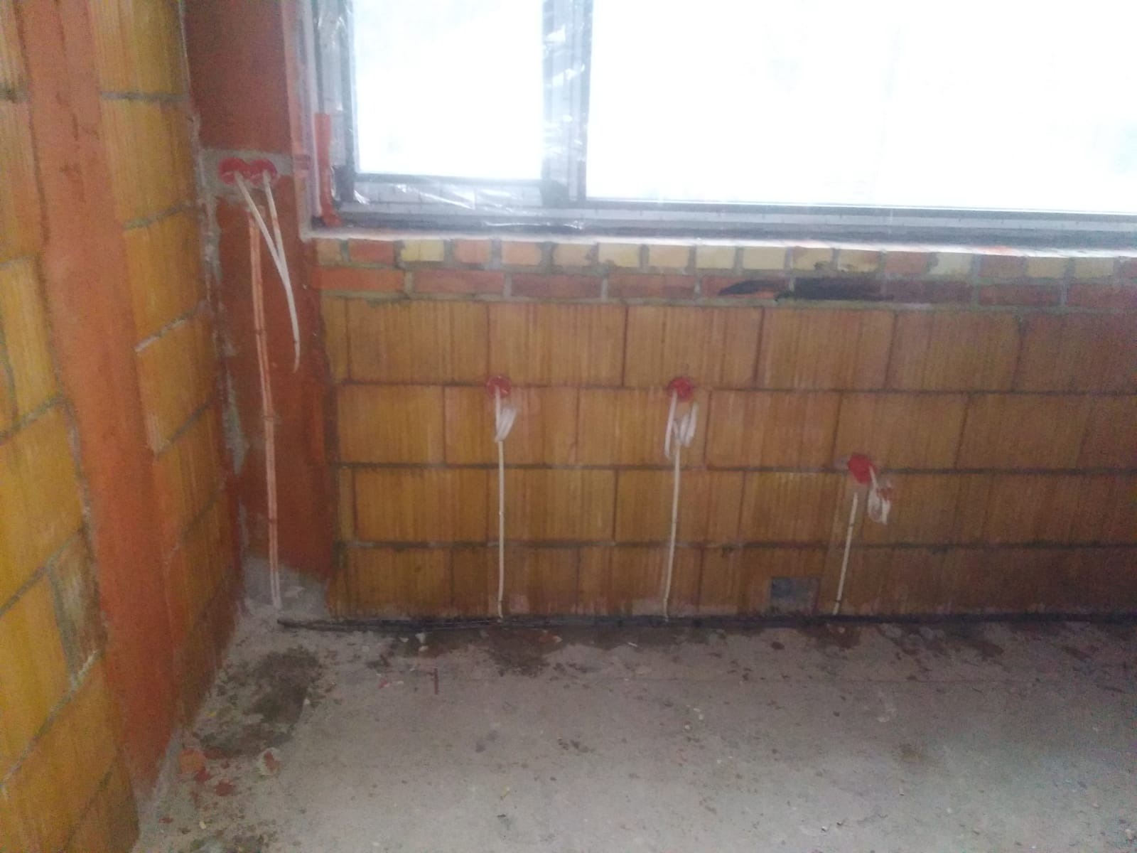 Wewnętrzna ściana z cegły z widocznymi przewodami elektrycznymi wystającymi ze ściany, przygotowanymi do dalszej instalacji, w surowym stanie wykończenia.