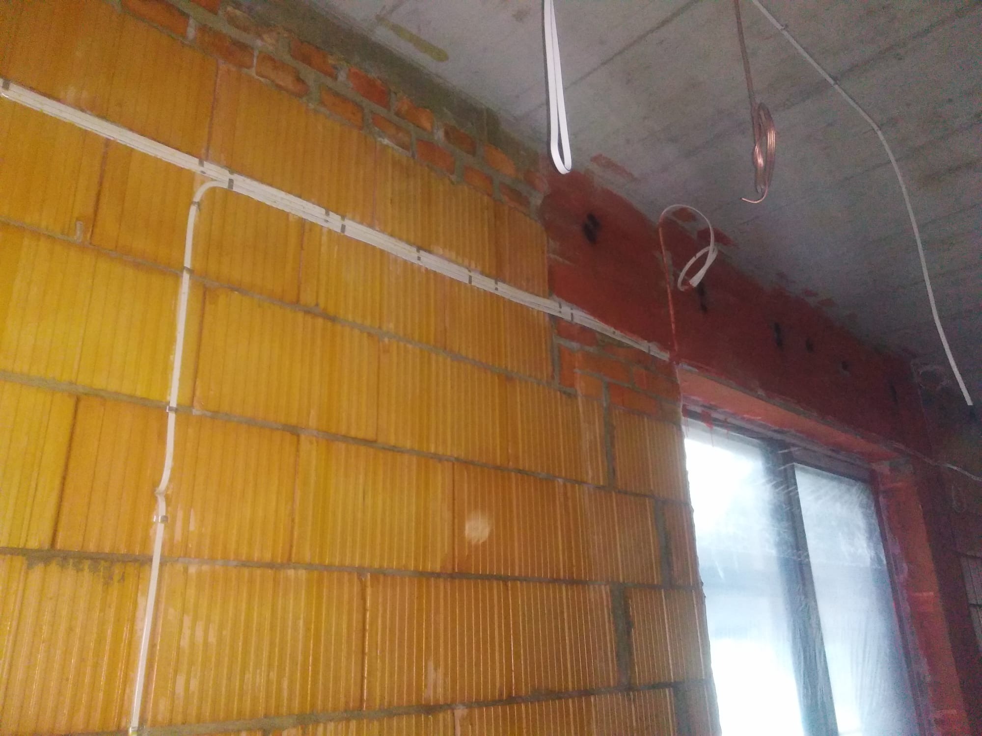 Montaż instalacji elektrycznej w surowym stanie: kable w białych listwach przymocowane do ściany z pustaków ceramicznych, przewody miedziane zwisające z sufitu.