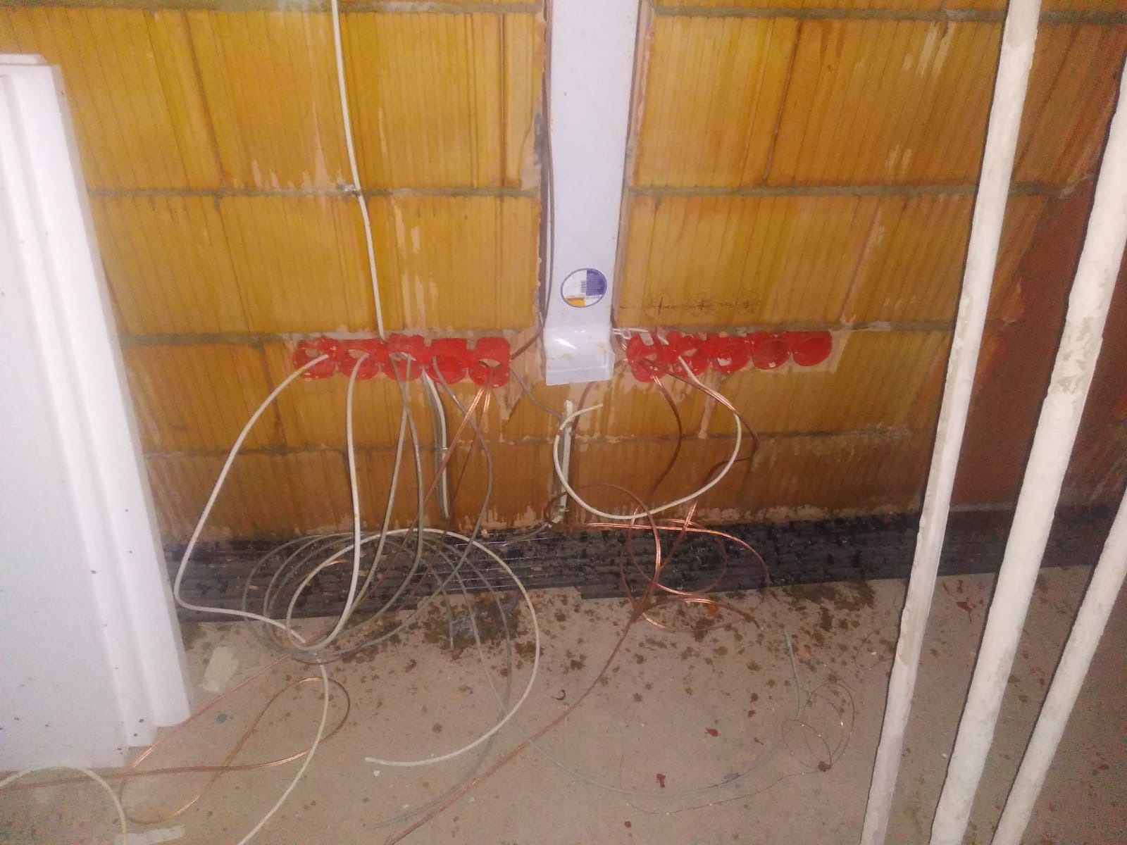 Instalacja elektryczna w trakcie montażu w nowym budynku w Warszawie. Widoczne czerwone puszki instalacyjne w ścianie z cegły, przewody elektryczne oraz biała skrzynka rozdzielcza.