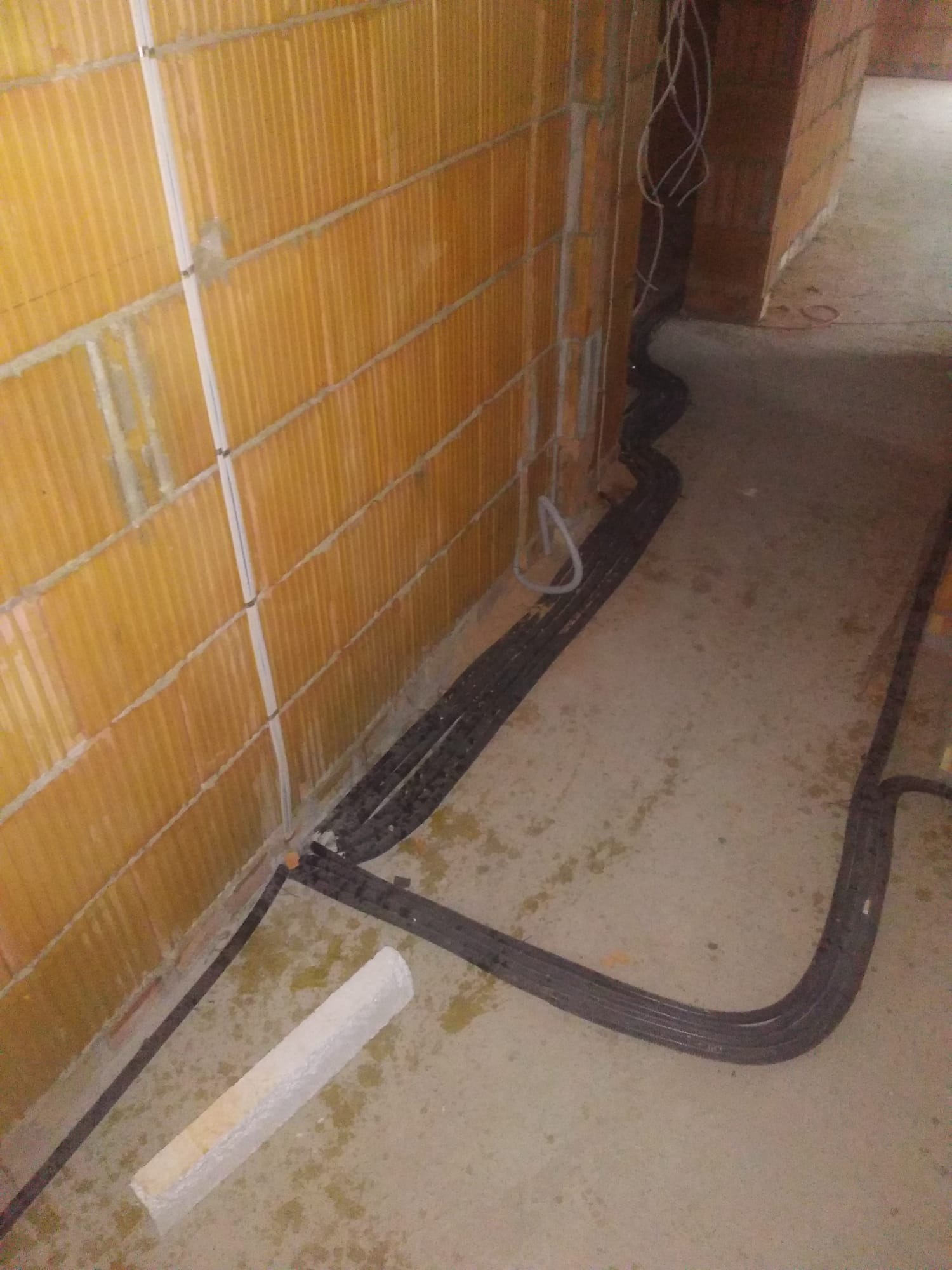 Układanie peszli z kablami elektrycznymi wzdłuż ceglanej ściany na surowym betonie w nowym budynku.