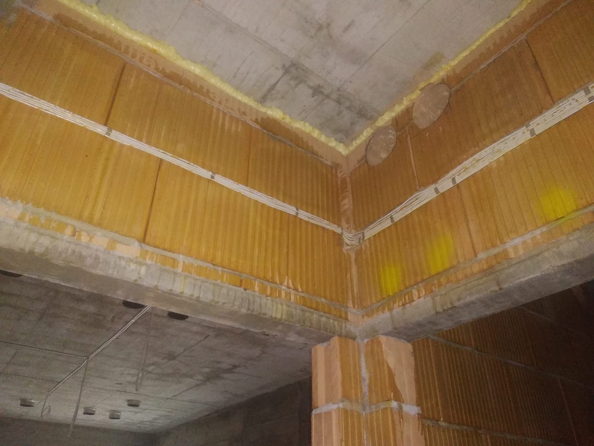 Surowy stan instalacji elektrycznej w budynku: przewody ułożone wzdłuż ścian z pustaków ceramicznych, zabezpieczone pianką montażową przy suficie betonowym.