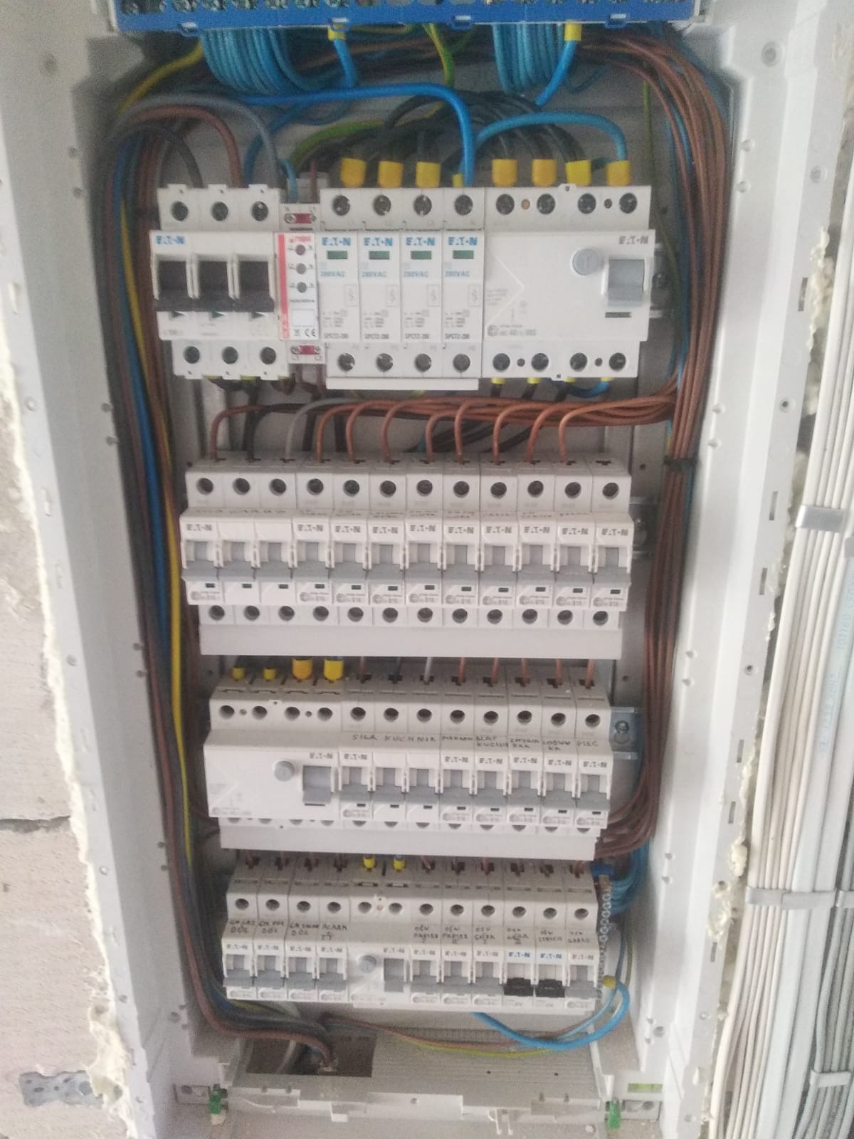 Rozdzielnica elektryczna z zainstalowanymi zabezpieczeniami różnicowoprądowymi i nadprądowymi marki EATON, widoczne przewody w różnych kolorach, zamontowana w surowym stanie wykończenia budynku.