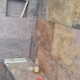 Ściana łazienki w trakcie wykańczania z kamienną okładziną, widoczna wnęka, poziomica, odkurzacz i butelka z napojem.