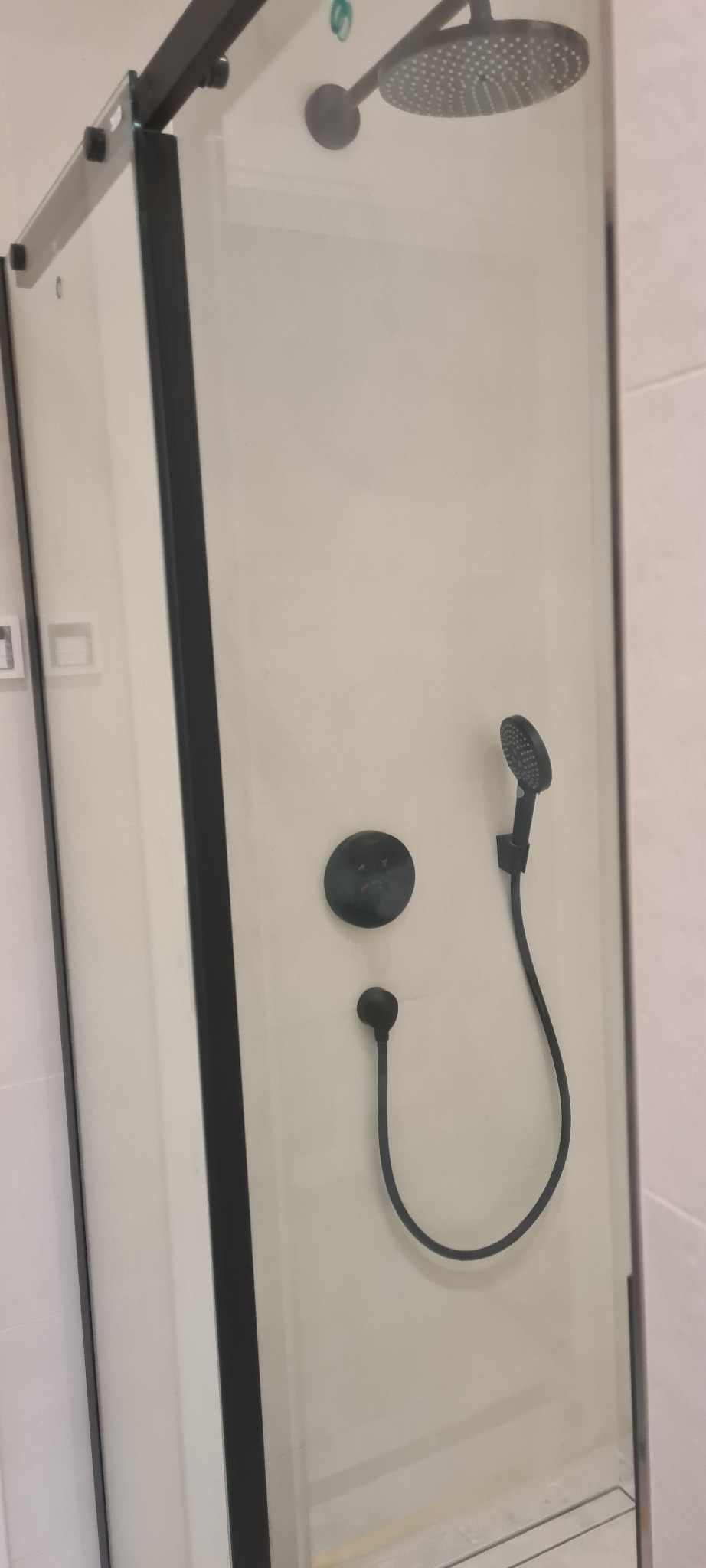 Nowoczesna kabina prysznicowa z czarnymi elementami, widoczna deszczownica, bateria podtynkowa i słuchawka prysznicowa na białym tle.