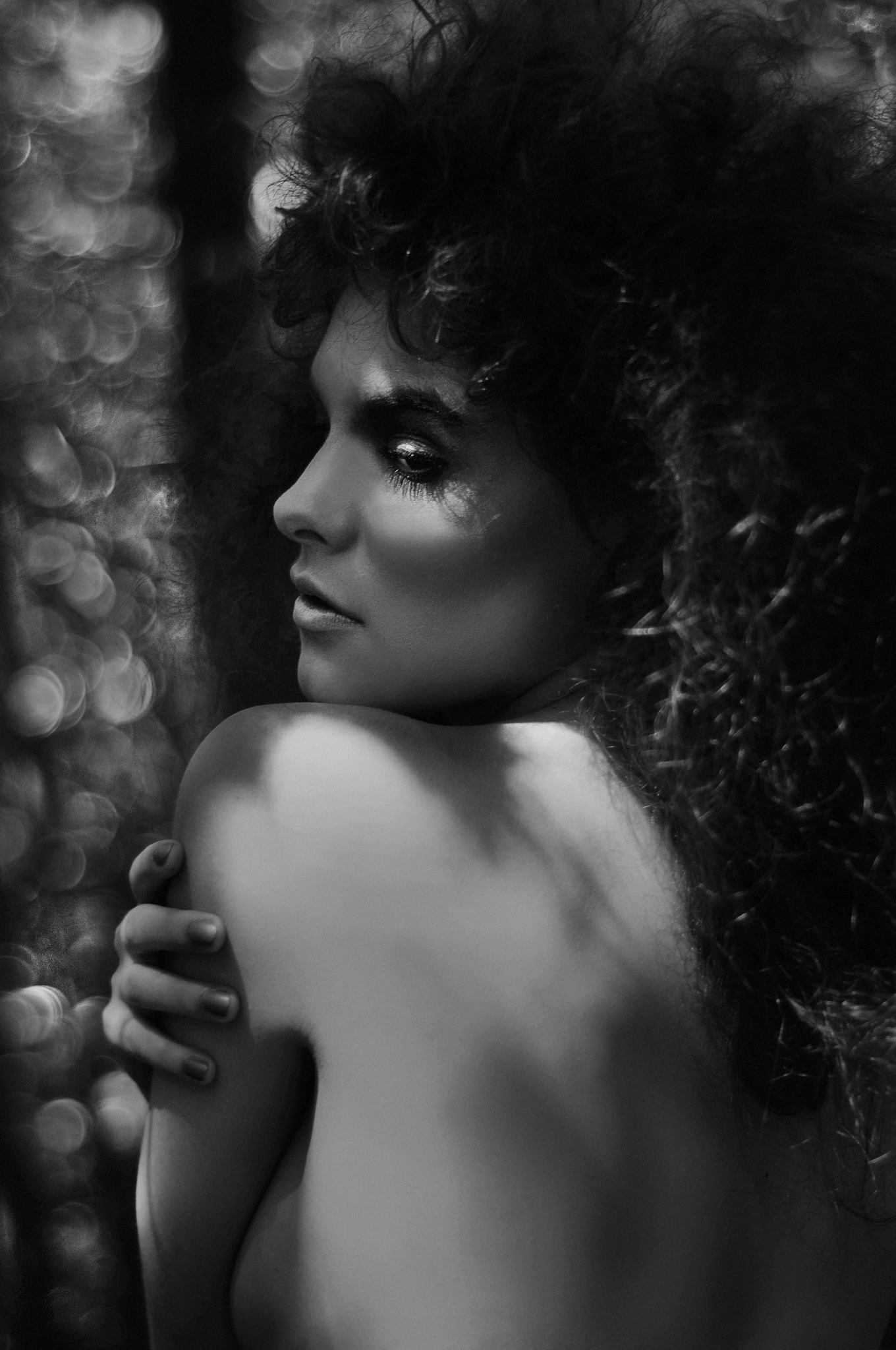 Czarno-biały portret kobiety z kręconymi włosami spoglądającej przez ramię, wykonany w Nysie, z efektem bokeh w tle.