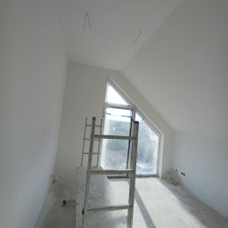Star-Sad - Poddasze po remoncie, świeżo pomalowane na biało, z zabezpieczonym oknem trójkątnym folią i rozstawionym rusztowaniem malarskim.