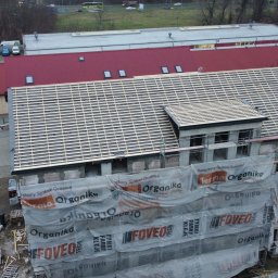 PROSTE DACHY USŁUGI CIESIELSKO-DEKARSKIE MARCIN KWIETNIEWSKI - Więźba dachowa w trakcie montażu na budynku w Gorzowie Wielkopolskim, widok z góry. Budynek w rusztowaniach, częściowo zakryty siatką ochronną.