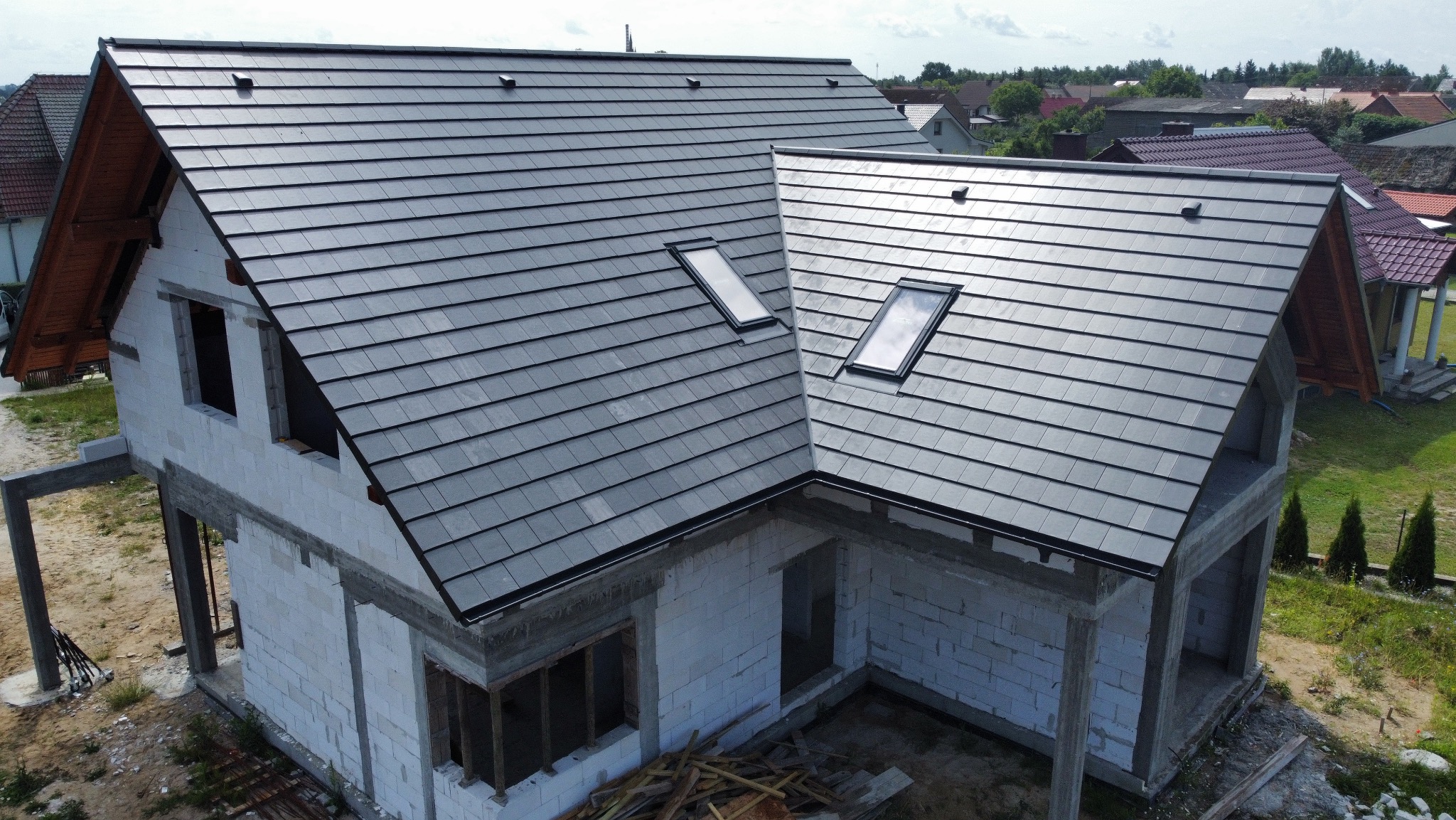 Dom w stanie surowym otwartym z szarą dachówką i oknami dachowymi. Widok z góry ukazuje regularny wzór ułożenia dachówek.