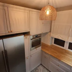 Jasnoszara kuchnia w stylu skandynawskim z drewnianym blatem, piekarnikiem w zabudowie i wiszącą lampą z plecionki, widok z góry.