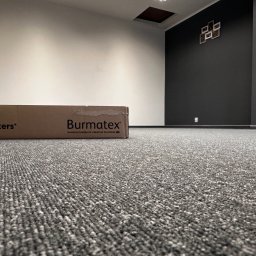 PERFORM SPÓŁKA Z OGRANICZONĄ ODPOWIEDZIALNOŚCIĄ - Szara wykładzina dywanowa w biurze z kartonem producenta Burmatex, widok z niskiej perspektywy.