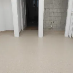 Beżowa podłoga z wykładziny w jasnym pomieszczeniu, widok z perspektywy, z fragmentem łazienki w tle.