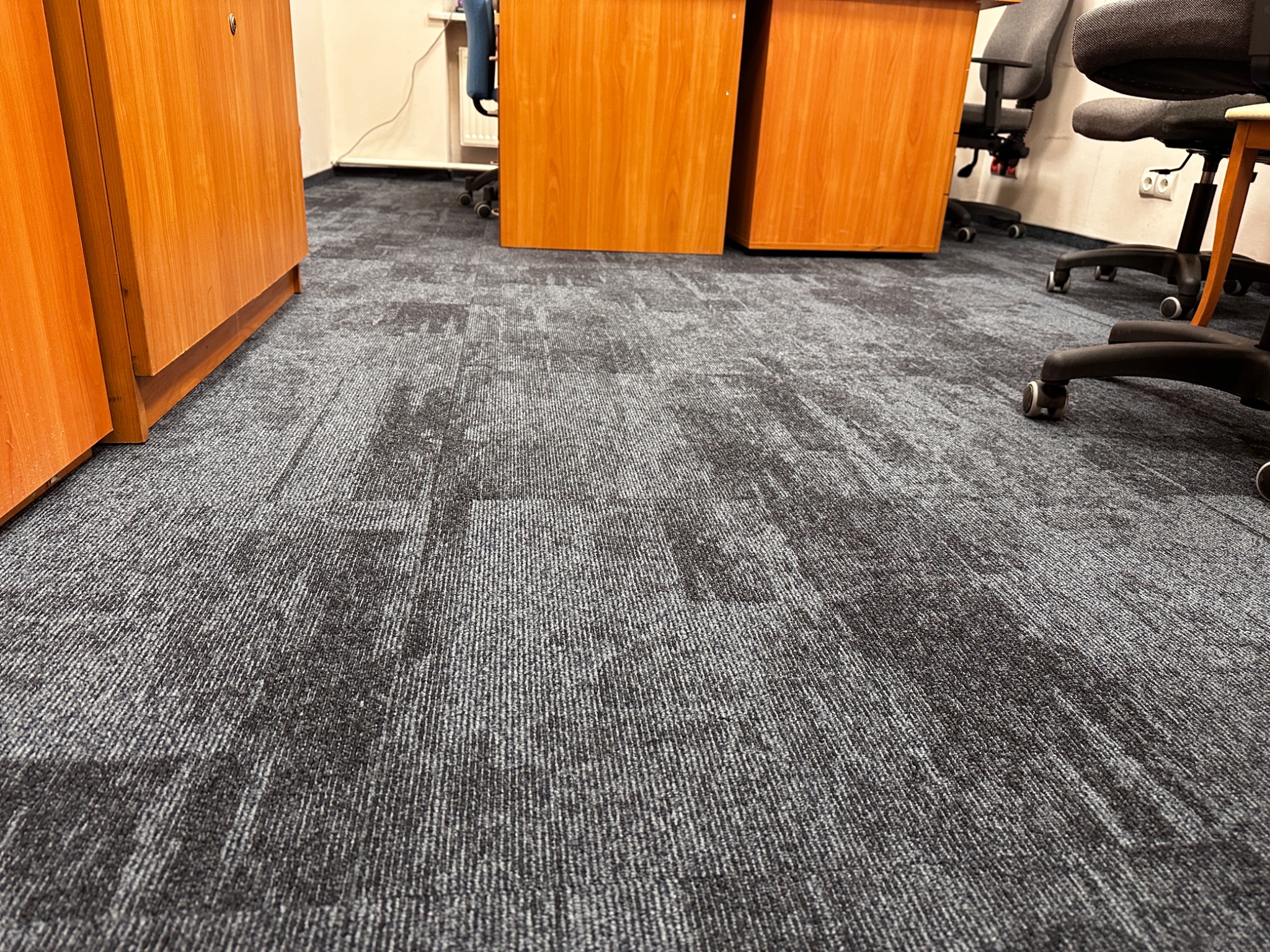 Szara wykładzina dywanowa w biurze, widok na podłogę pomiędzy biurkami i krzesłami na kółkach.
