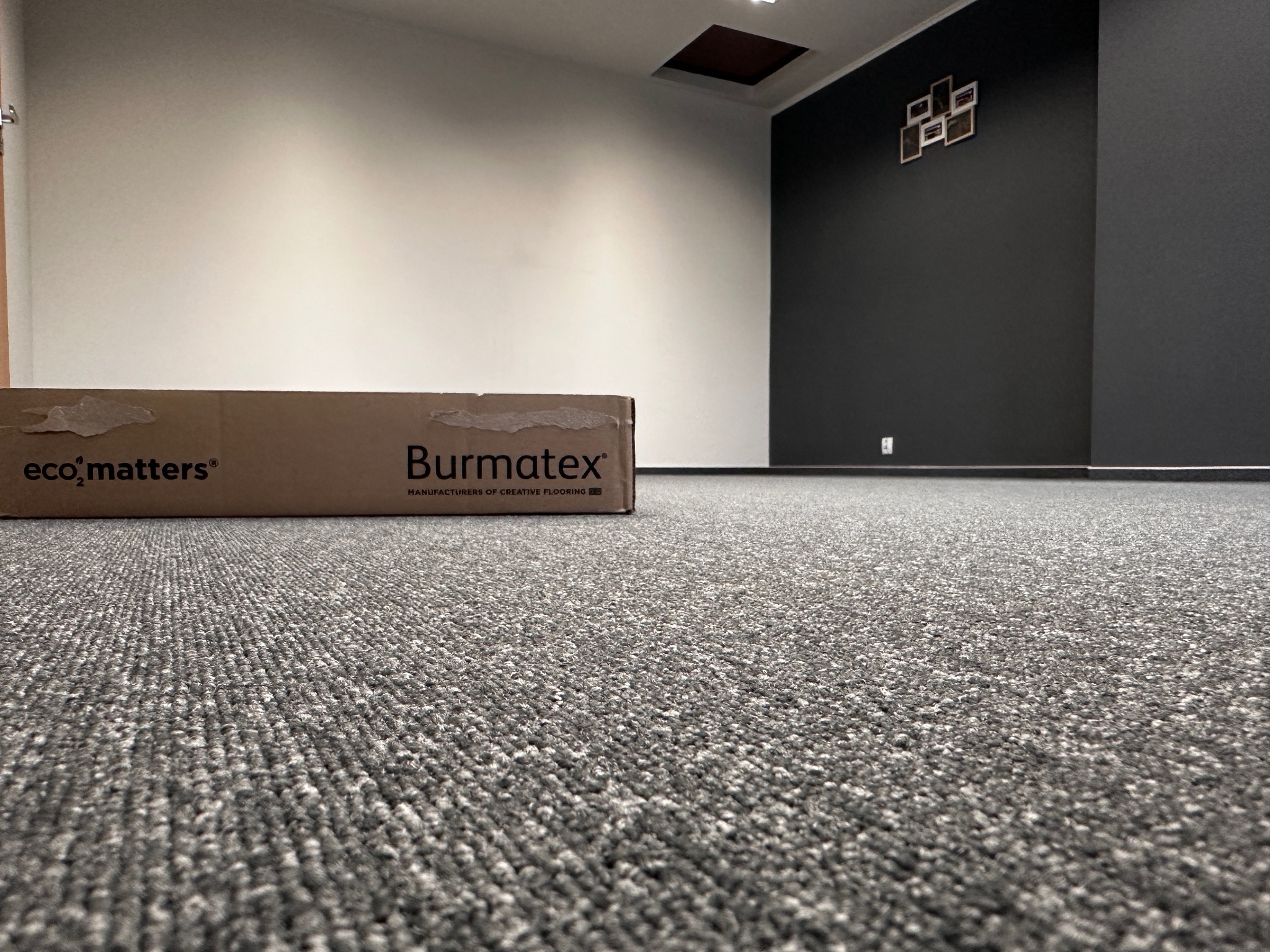 Szara wykładzina dywanowa w biurze z kartonem producenta Burmatex, widok z niskiej perspektywy.