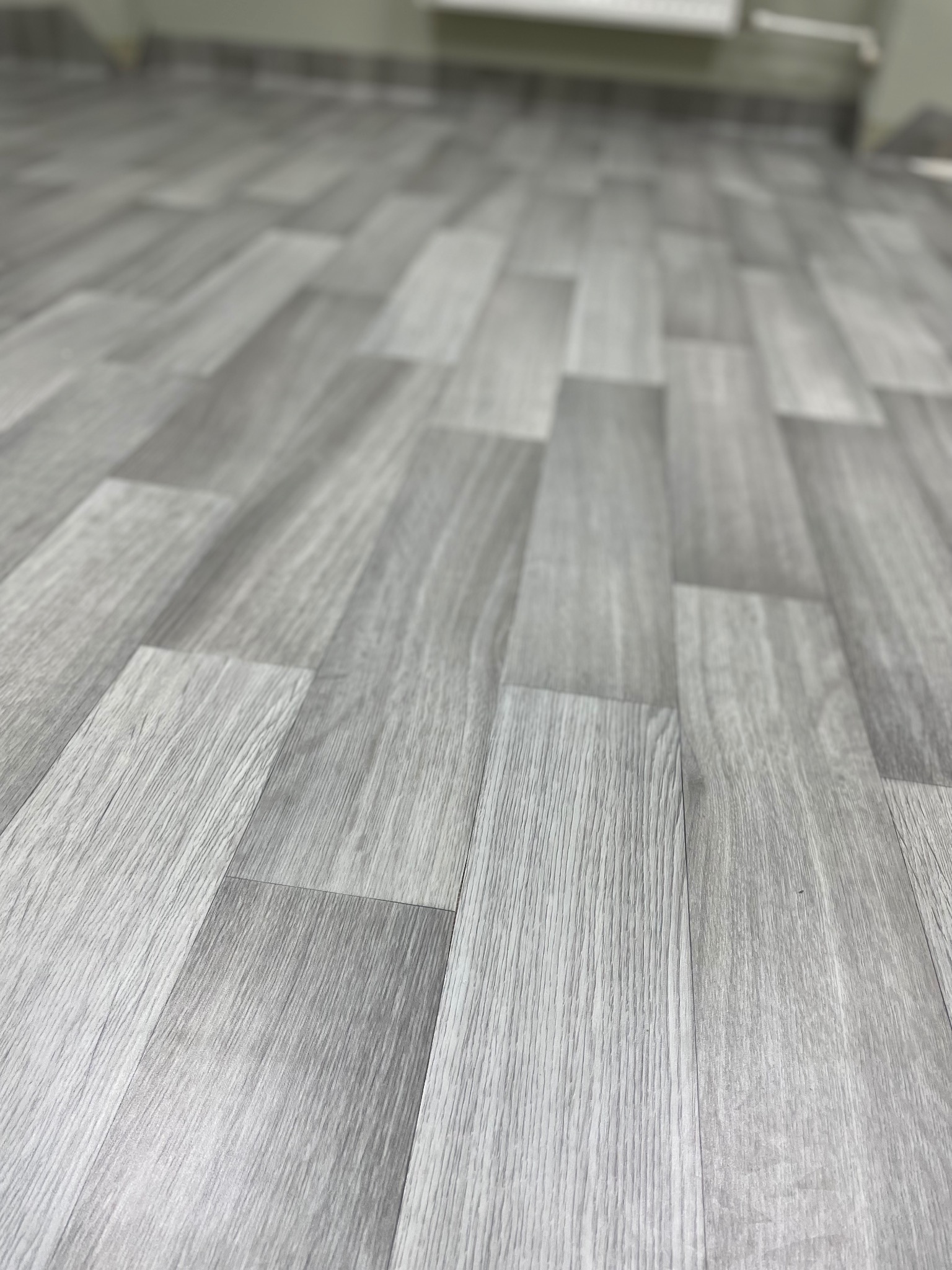 Szare panele podłogowe ułożone w jodełkę, widoczne z niskiej perspektywy, z delikatnym efektem rozmycia w tle.