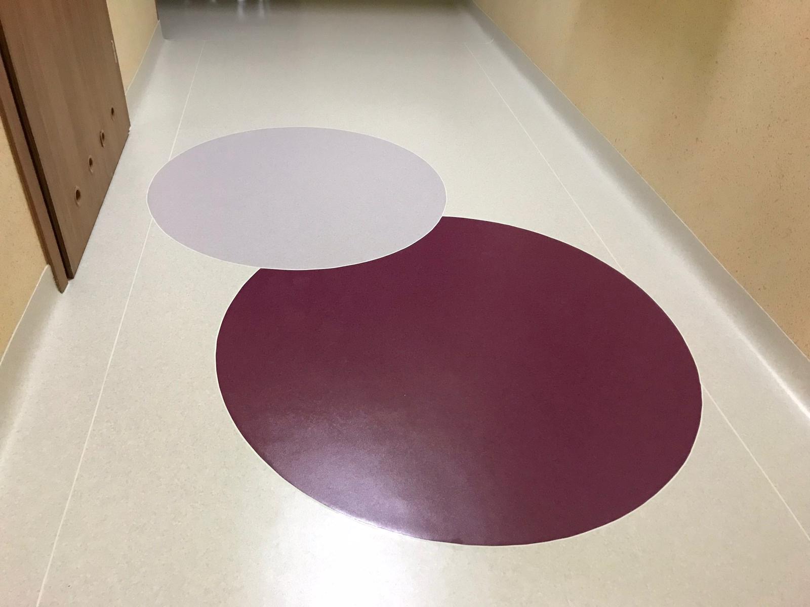 Korytarz z jasną wykładziną, na której widnieją dwa naklejone okręgi: jasnoszary i bordowy.