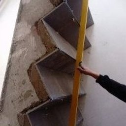 Usługi Remontowe Robert Balcerzak - Montaż półek schodkowych na surowej ścianie, sprawdzane poziomicą, widoczne niedoskonałości podłoża.