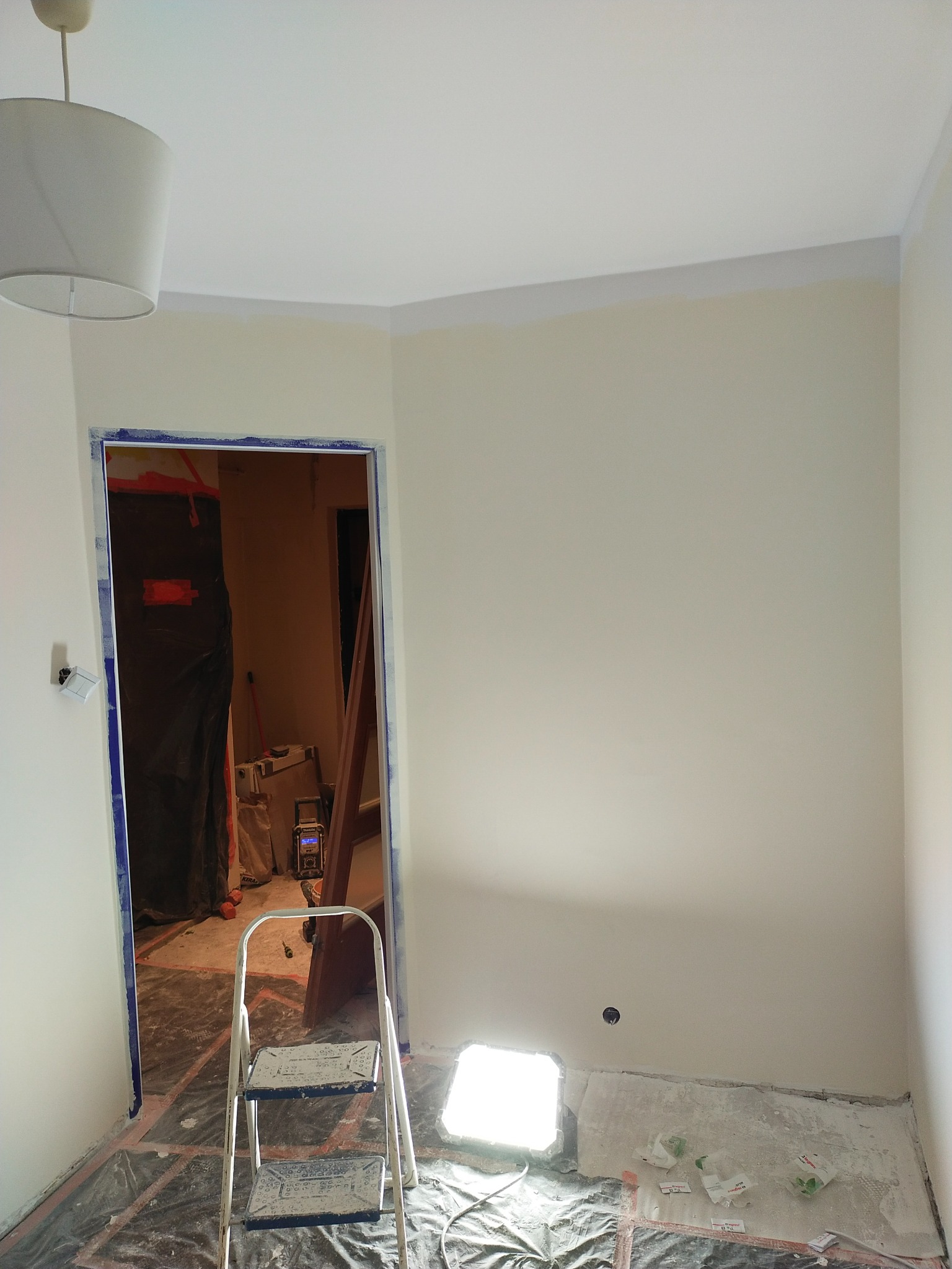 Świeżo pomalowane jasne ściany w pokoju z zabezpieczonymi folią podłogami, widoczna drabina malarska i oświetlenie robocze, przygotowane do dalszych prac wykończeniowych.