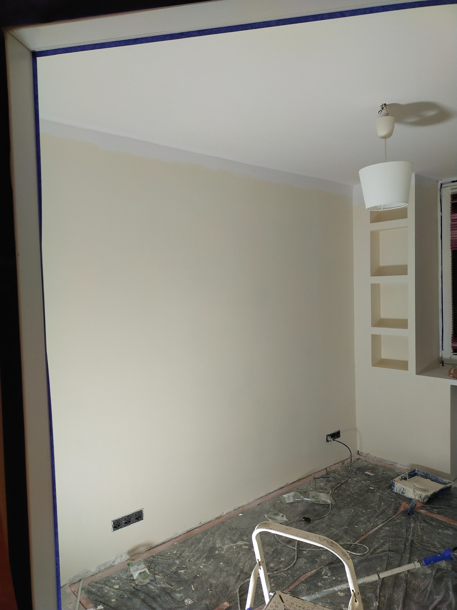 Świeżo pomalowany pokój z zabezpieczoną taśmą sufitową i folią ochronną na podłodze, widoczna drabina malarska i puszka z farbą.