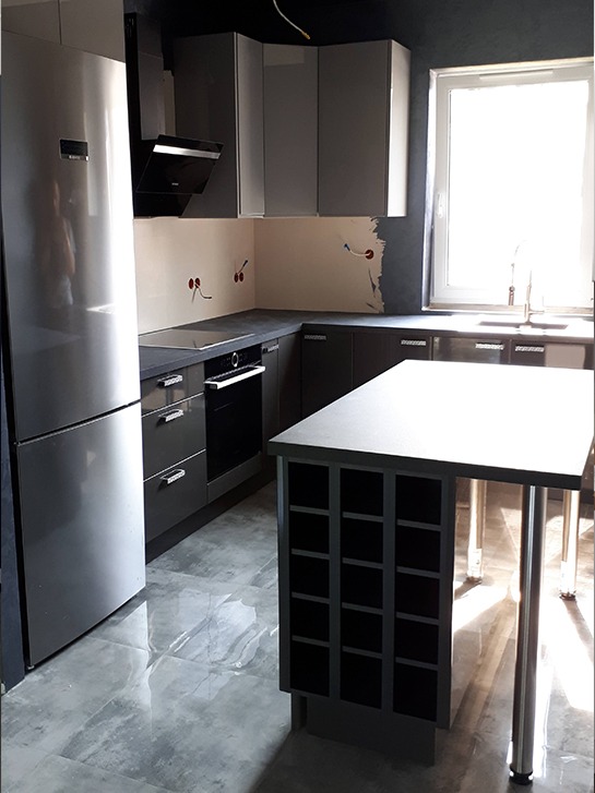 Szara kuchnia z wyspą w trakcie montażu, widoczne niedokończone ściany i wystające kable elektryczne, błyszcząca podłoga, nowoczesny design.