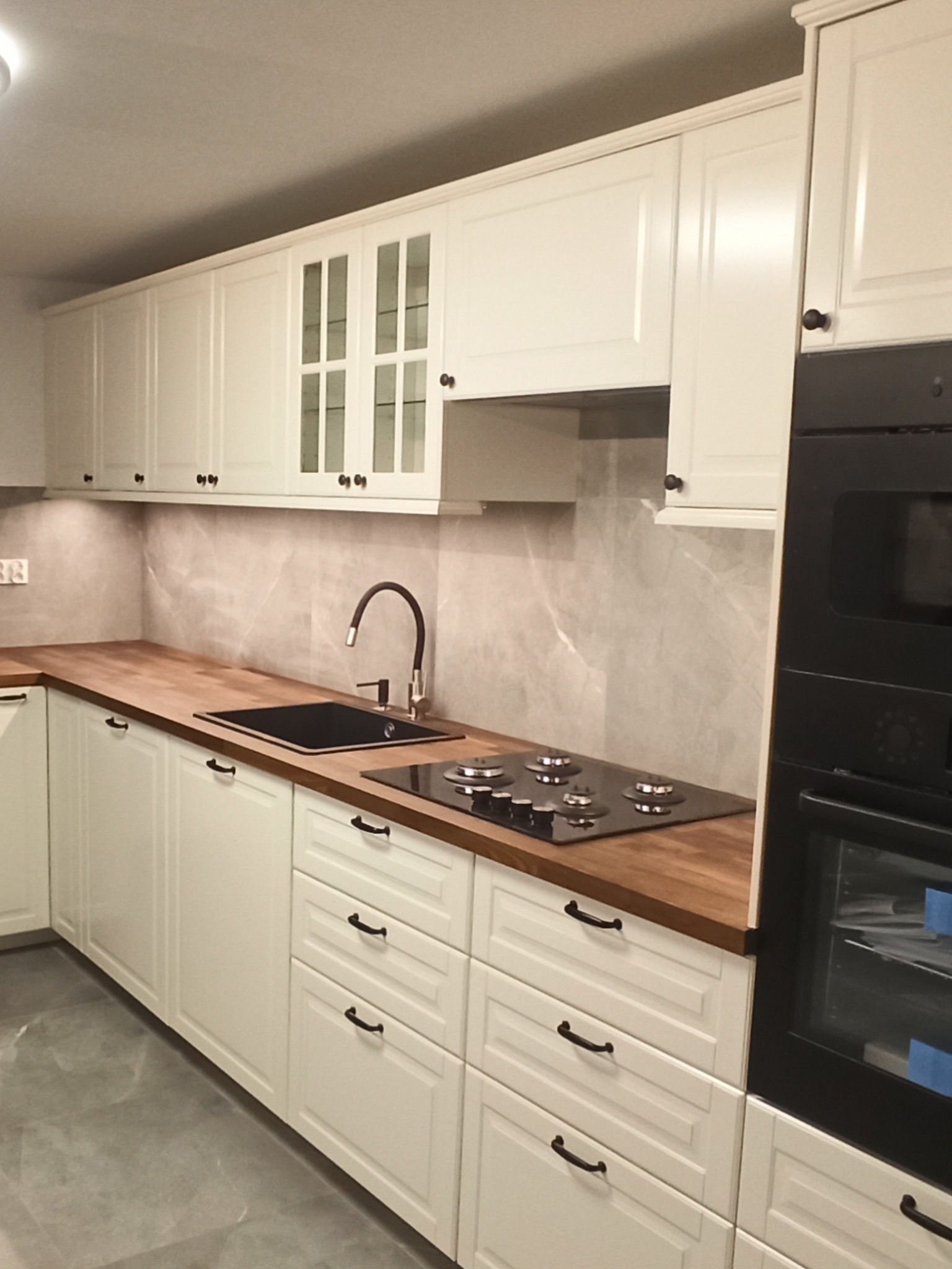 Jasna zabudowa kuchenna z drewnianym blatem w mieszkaniu w Warszawie, widoczna płyta grzewcza i piekarnik.