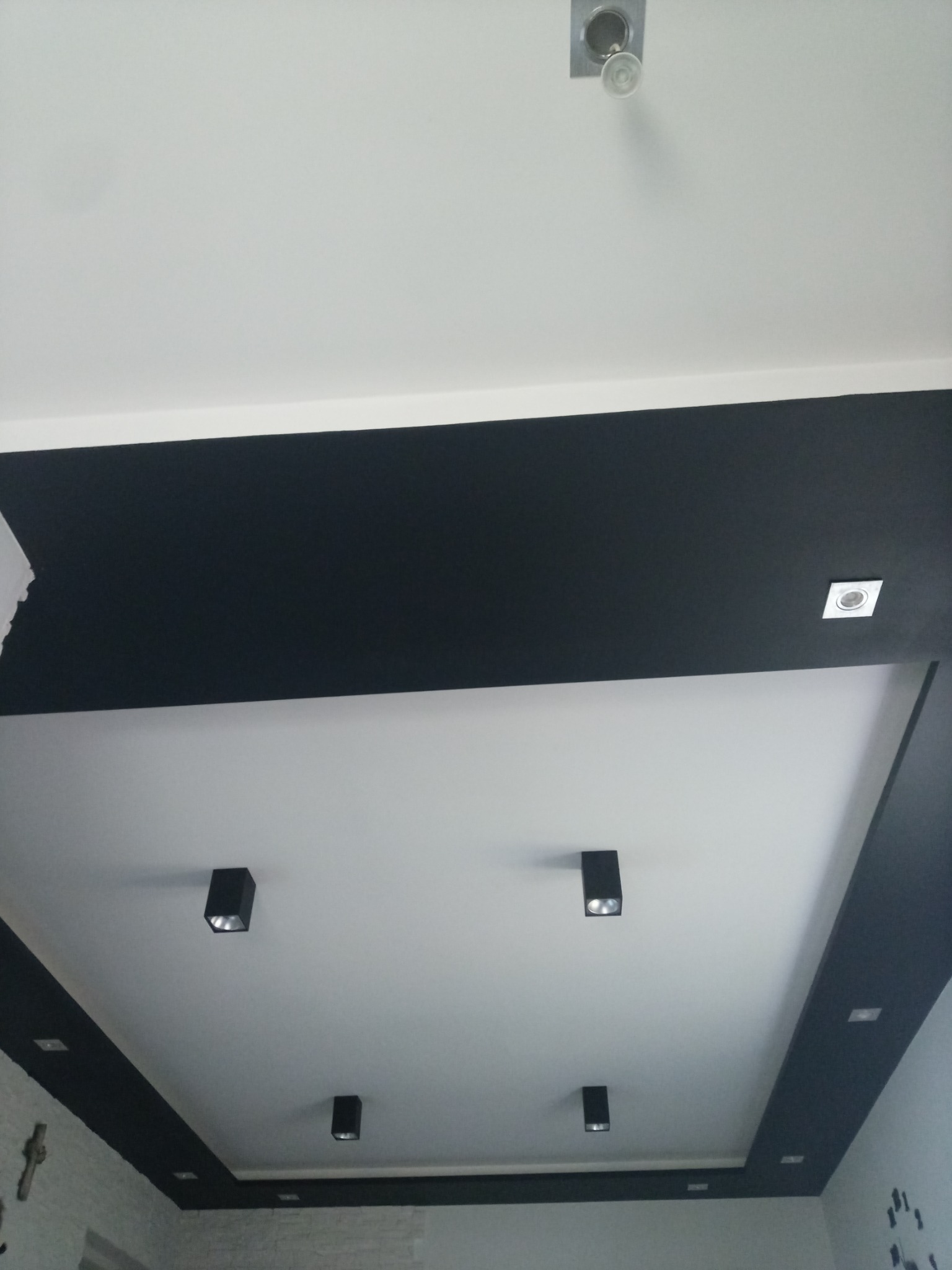 Nowoczesny, biały sufit z czarnymi wstawkami i punktowym oświetleniem w kształcie kostek, widoczny fragment ściany z dekoracyjną cegłą.