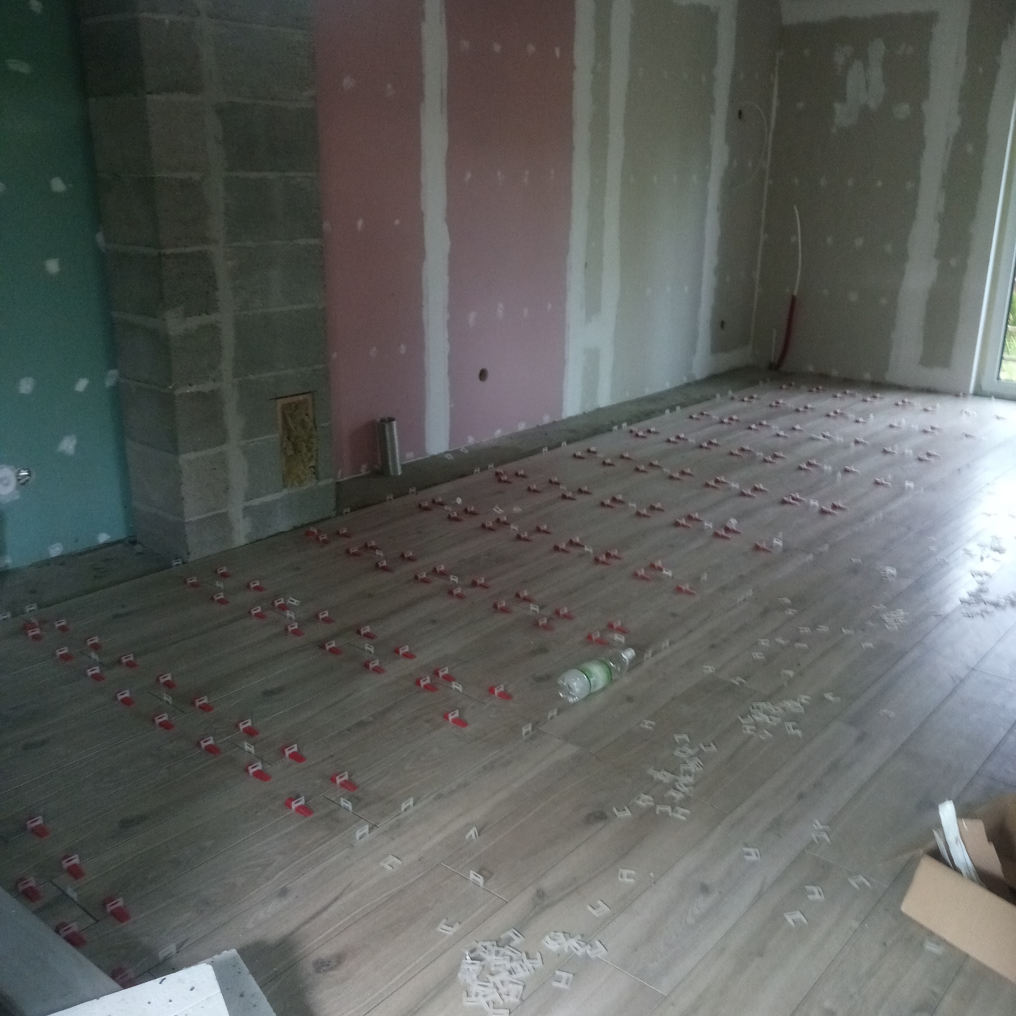 Układanie podłogi z paneli imitujących drewno w trakcie prac wykończeniowych, widoczne płytki dystansowe i butelka wody na podłodze, ściany w stanie surowym.