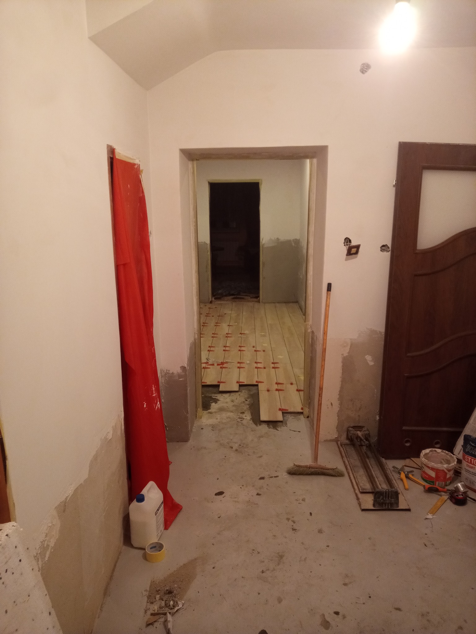 Korytarz w trakcie układania parkietu z widocznymi płytkami, krzyżykami dystansowymi, narzędziami do cięcia i przygotowania podłoża.