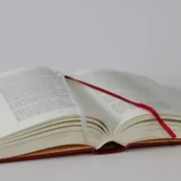 Otwarta książka w twardej oprawie z czerwoną i białą zakładką na białym tle.