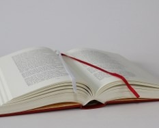 Otwarta książka w twardej oprawie z czerwoną i białą zakładką na białym tle.