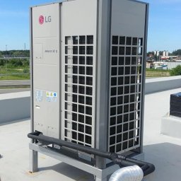 ART COOL Adam Czerwński - Kompaktowa, zewnętrzna jednostka klimatyzacyjna LG Multi V 5 na dachu, z widocznymi przewodami i narzędziami, sugerująca montaż lub serwis. Błękitne niebo w tle.