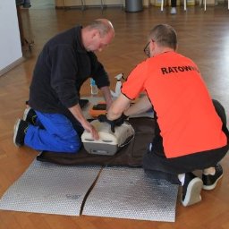 Sela Sp. z o.o. - Instruktorzy demonstrują użycie defibrylatora AED na manekinie podczas zajęć, jeden w pomarańczowej koszulce z napisem 'RATOWNIK'.