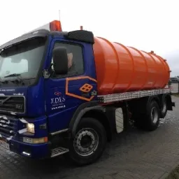 Ciężarówka asenizacyjna Volvo FM7 z pomarańczową cysterną, zaparkowana na brukowanym placu, z widocznym logo firmy EDES na niebieskiej kabinie.